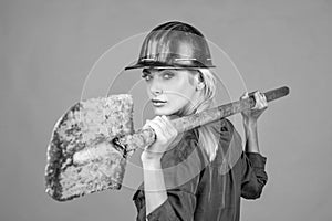 woman engineer in protective helmet and boilersuit hold shovel on orange background, engineering
