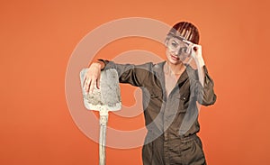 woman engineer in protective helmet and boilersuit hold shovel on orange background, industry