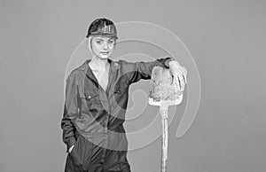 woman engineer in protective helmet and boilersuit hold shovel on orange background, industry