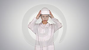 Woman engineer in white robe and white hard hat walking on gradient background.