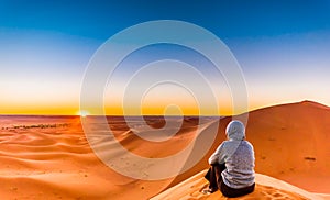 Woman enjoing sunrise in the Sahara desert next to M`hamid in Mo