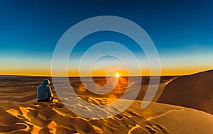 Woman enjoing sunrise in the Sahara desert next to M`hamid in Mo