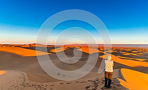 Woman enjoing sunrise in the Sahara desert next to M`hamid in Mo