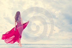 Woman enjoy Sun Sea on Beach. Girl Rear Side Back View in Red Flying Dress on Wind. Happy Holiday Vacation. Wellbeing Lifestyle