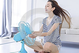 Woman enjoying air flow from fan on floor iat home. Summer heat concept photo