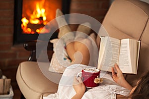 Woman enjoying a book and a hot chocolate drink by lying the fir