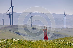 Woman enjoying clean air on the green meadow with wind turbines on the background