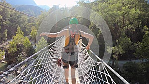 Woman enjoying extreme adventure crossing canyon river by rope bridge