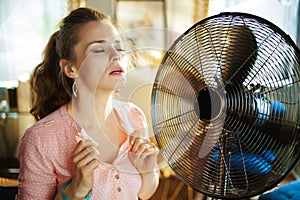 Woman enjoying freshness near fan suffering from summer heat
