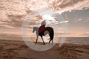 Woman enjoying a leisurely ride on horseback along a beach at sunset