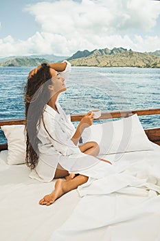 Woman enjoying morning coffee on boat. Bed on board. Travel, freedom lifestyle