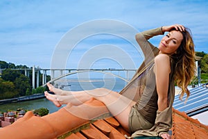 Woman enjoying sunbath on the rooftop on river bridge background.