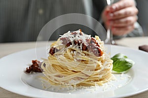 Woman enjoying tasty spaghetti with sun-dried tomatoes and parmesan cheese and wine at table in restaurant, closeup.