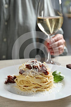 Woman enjoying tasty spaghetti with sun-dried tomatoes and cheese and wine at wooden table in restaurant, closeup.