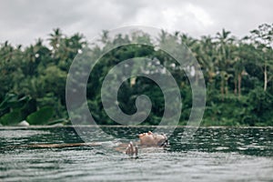 Woman enjoying tropical rain while swimming in infinity pool on Bali