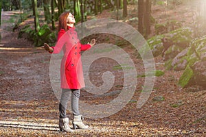 Woman enjoying the warmth of winter sunlight alone on forest park path with arms open