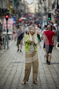 A woman enjoys music on headphones on a crowded street.