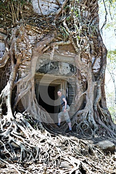 woman at an entrance to the destroyed covered with roots of trees temple Prasat Chrap in the Koh Ker temple complex, Siem Reap, C