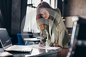 Woman entrepreneur stands and writes leaning on desk