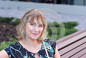 Woman, a European, middle-aged, 50-55 years old, a pretty blonde, sitting on a park bench