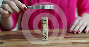 Woman evaluates risk from wooden cubes with magnifying glass