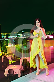 Woman in evening dress holding cocktail over night city background