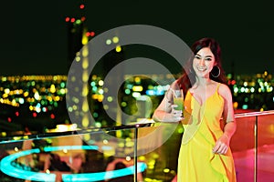 Woman in evening dress holding cocktail over night city background