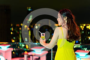 Woman in evening dress holding cocktail over night city background