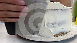 Woman evenly spreads the cream on the surface of the cake with a spatula