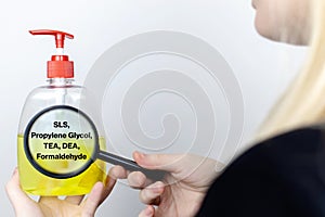 A woman examines the harmful ingredients of the liquid soap a magnifying glass. Harmful composition of ingredients. Means with SLS