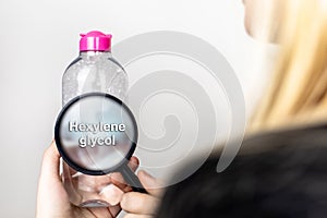 A woman examines the harmful ingredients of the micellar waterthrough a magnifying glass. Means with hexylene glycol. The concept