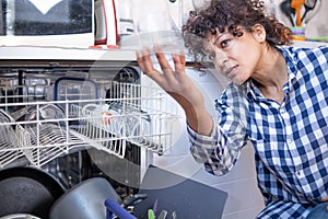 Woman examining dishwasher and glasses cleanliness