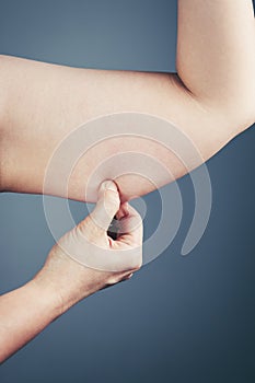 Woman with the excessive fat checking her upper arm, grey background.