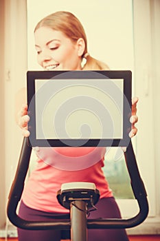 Woman on exercise bike holding pc tablet copyspace