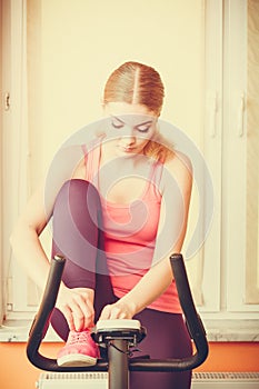 Woman on exercise bike tying lacing shoes.