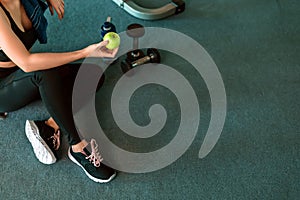 Woman exercise in gym fitness breaking and relax. hand  holding apple fruit after training sport and dumbbell, water bottle on the