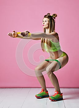 Woman exercising doing postnatal workout. Female fitness instructor working out with a rubber resistance band on modern pink