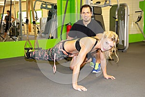 Woman exercising with gym coach man suspension straps in fitness club training