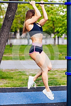 Woman exercising on horizontal bar outdoors in the summer.