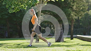 A woman is exercising in a park, holding a cup in her hand