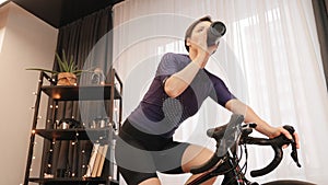 Woman is exercising on stationary bicycle. Female athlete is cycling on indoor smart trainer. Cyclist rides exercise bike at home,