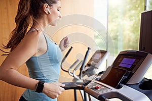 Woman Exercising On Treadmill At Home Wearing Wireless Earphones Checking Smart Watch