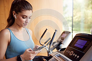 Woman Exercising On Treadmill Wearing Wireless Earphones And Smart Watch Checking Mobile Phone