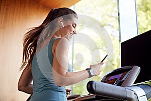 Woman Exercising On Treadmill Wearing Wireless Earphones And Smart Watch Checking Mobile Phone