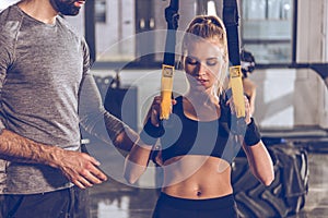 Woman exercising with trx gym equipment with trainer near by