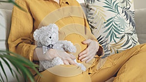 Woman expecting baby. Pregnant girl hugging belly and teddy bear toy resting, awaiting the child birth. Family planning