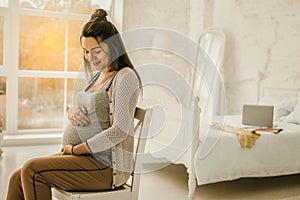 Woman expecting a baby is sitting in the bedroom
