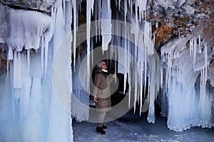 A woman explores huge icicles in the ice cave of Oltrek Island. Winter trip on the frozen Lake Baikal