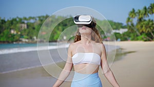 Woman explores tropical beach in VR, waves lapping nearby. Immersed in virtual reality, she experiences digital worlds