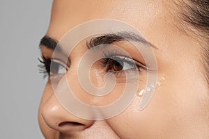 Woman with eye cream on grey background, closeup. Skin care
